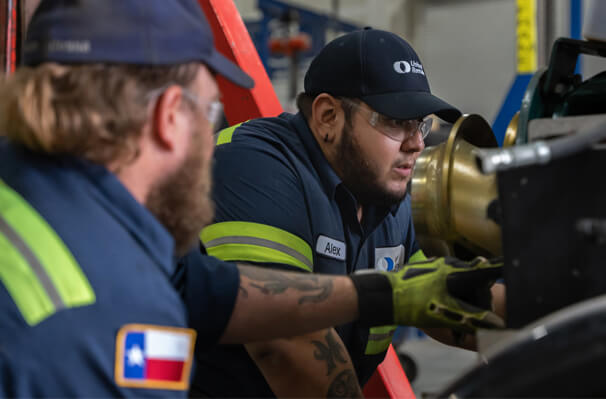Two male maintenance workers in navy-blue United Rentals uniforms examine some equipment.